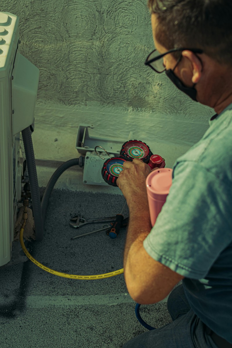 An HVAC technician using a refrigerant manifold gauge set to diagnose an outdoor AC unit.
